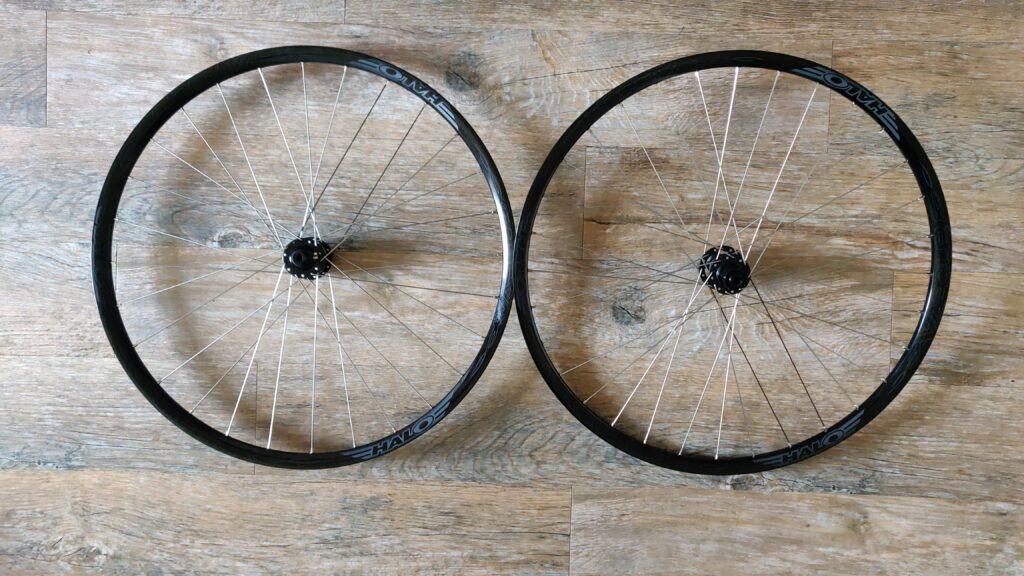 A pair of 700c bicycle wheels with a wooden floor in the background.
